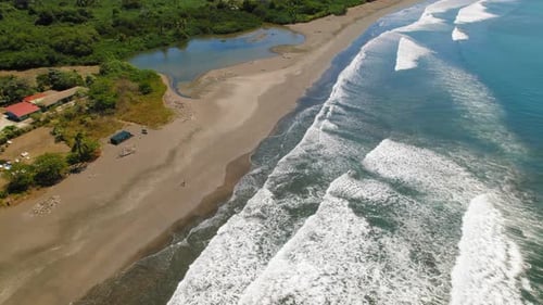 Aerial view of tropical sandy beach and waves near small resort in Costa Rica