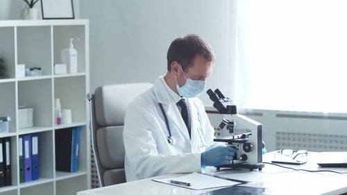 Professional Medical Doctor Working in Hospital Office Using Microscope