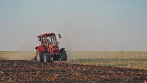 Red tractor at work. Agricultural machine plowing the field at daytime.