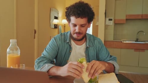 Young Adult Man Enjoys Sandwich at Table