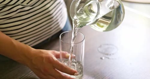 Close Up of Woman Pouring Fresh Clean Water Into Glass From Jug at Home