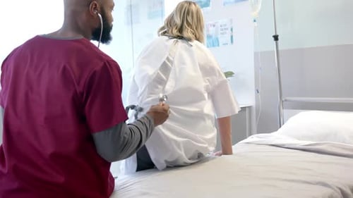African american male doctor with stethoscope examining caucasian female patient at hospital