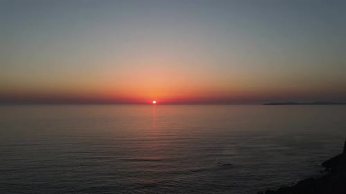 Drone air footage of young friends watching the sun setting on the horizon from a cliff by the sea i