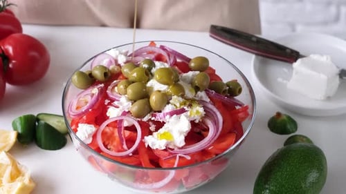 Woman pouring olive oil to bowl of Greek salad