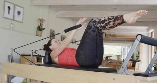 Fit senior caucasian woman stretching on reformer in pilates studio, unaltered, in slow motion