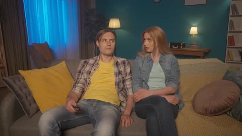A Couple are Watching TV The Man Switches Channels with the Remote Control Stops The Woman Takes the