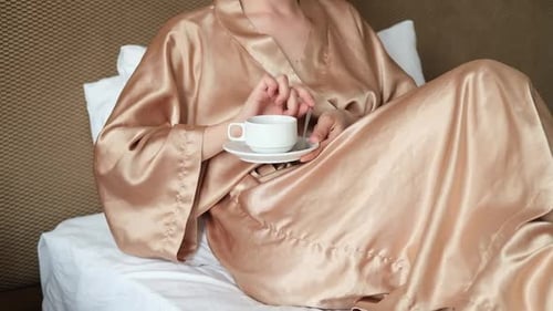 Beautiful Caucasian Woman is Sitting on White Bed in Bedroom at Home or Hotel and Having Rest in the