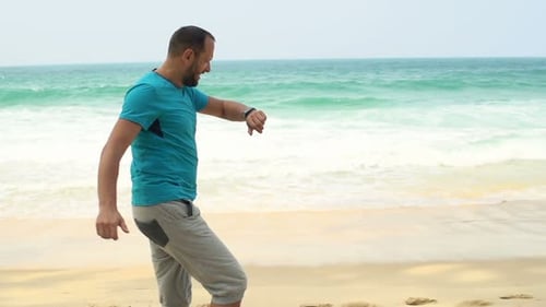 Handsome young man checks pulse on smartwatch after jogging on tropical beach in slow motion