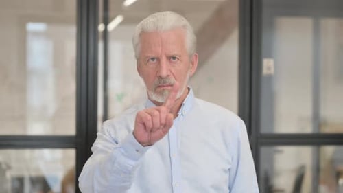 Senior Man Signaling No with Finger in Office