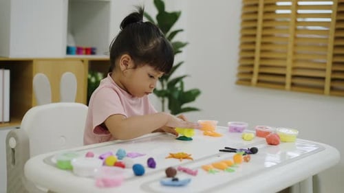 Little Girl Plays with Colorful Modeling Clay at Table