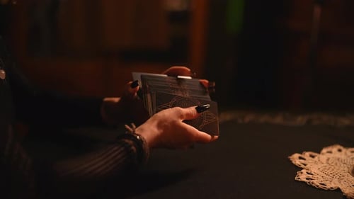 Nahaufnahme: Hände einer unkenntlichen Wahrsagerin mit schwarzen Nägeln beim Mischen von Tarotkarten, Vorbereitung für