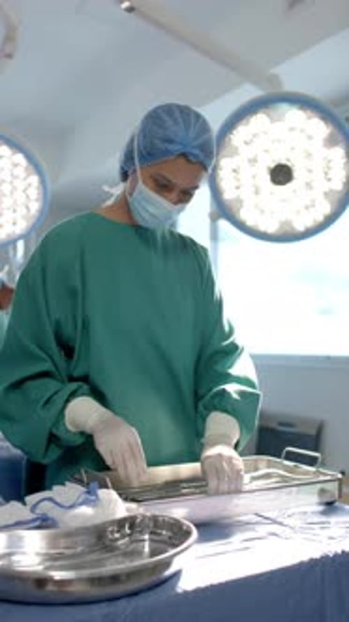 Vertical video of biracial female surgeon preparing surgical instruments in theatre, slow motion