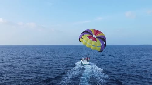 Motorboat Launching Parasailing Couple into The Sky Over Blue Ocean, Drone Back View