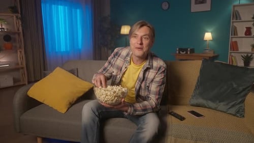 A Man Sits on the Couch in the Evening Eats Popcorn and Watches TV A Man Watches a Comedy a Comedy