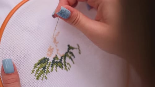 Close Up Hand View Of Woman Embroidering Pattern With Blue Nails On Fabric