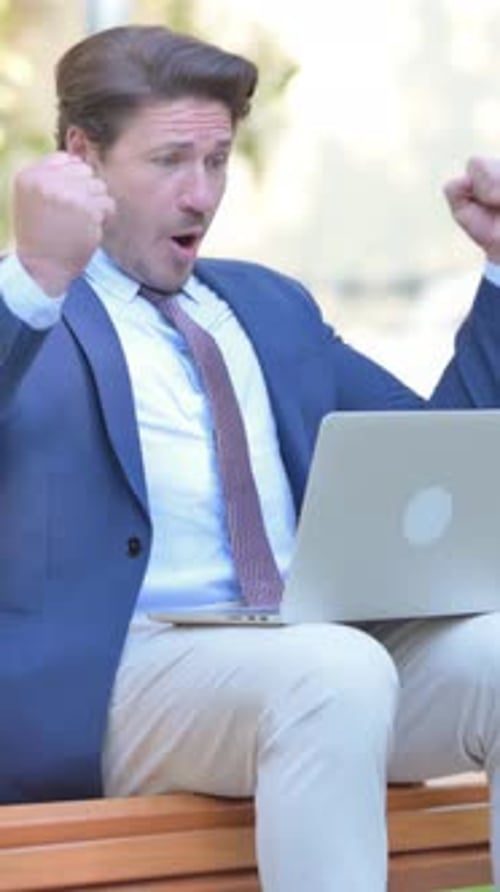 Excited Man Cheers at Laptop While Sitting Outside