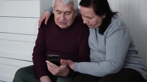 Old Couple Using a Phone Together While Relaxing in the Kitchen at Home Elderly Man and Woman