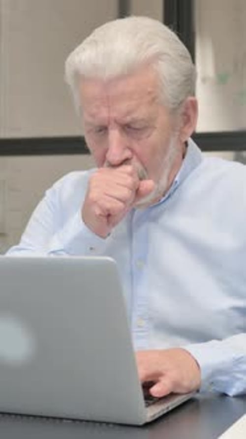 Coughing Senior Businessman Using Laptop in Office