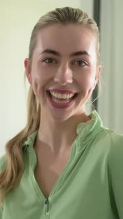 Vidéo verticale : Femme souriante après le signal, souriant pour rire, inclinée, se retournant à la maison, fermeture éclair verte