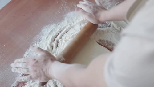 A baker rolls out dough with a wooden rolling pin and begins to prepare bread and pizza.