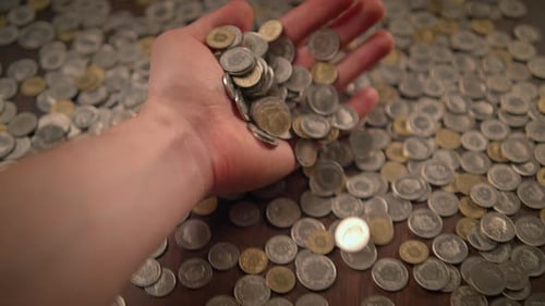 Hand Holding and Releasing Coins Over Pile