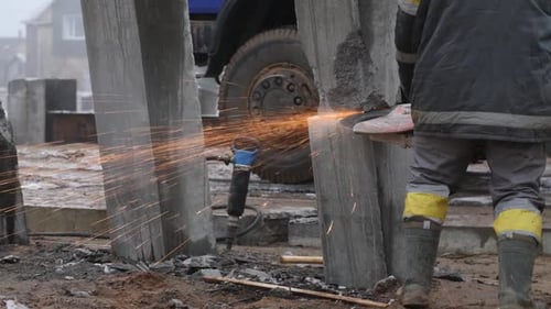 Worker cutting concrete piles with cutter or circular saw on construction site