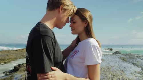 Affectionate young couple embracing on rocky beach during daytime