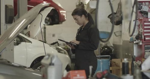 Female car mechanic looking under vehicle using digital tablet in automotive workshop