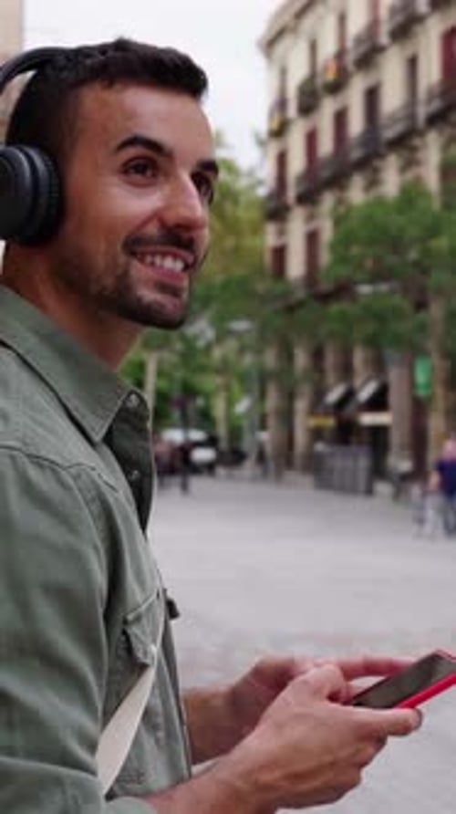 Handsome Man Relaxing Outdoors Using Phone and Listening Music in a City Street