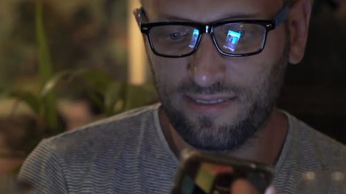 Young Man Texting on Smartphone Sitting in Cafe at Night 30s
