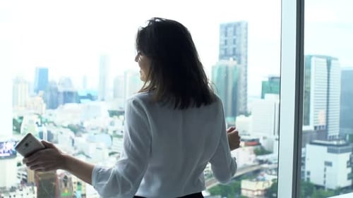 Businesswoman Listening to Music and Dancing by Window in Office 30s