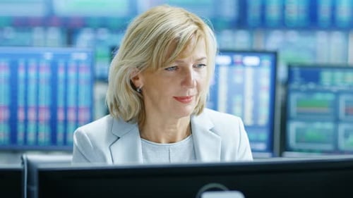 Portrait of the Senior Female Stock Trader Operating at Her Workstation. Behind Her Multiple Monito