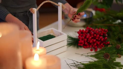Inspired Young Unrecognizable Woman Making Handmade Christmas Basket with Green Fir Branch and Red
