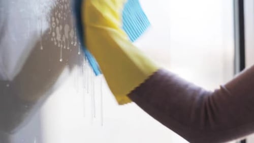 People, Housework and Housekeeping Concept - Woman in Gloves Cleaning Window With