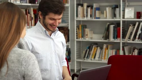Male Student Enthusiastically Shows His Female Classmate Something on a Laptop in the Library