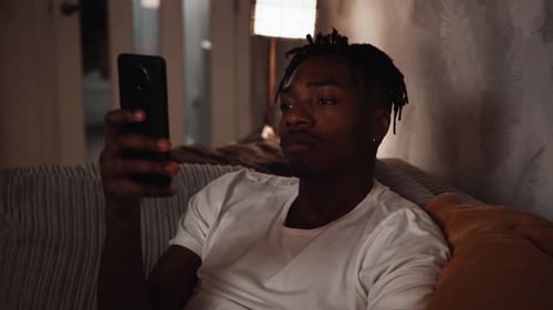 Young black male sitting on the sofa at home using a smart phone