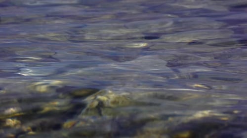 Liquid texture of lake water reflecting sunlight on shore with pebbles