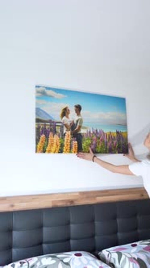 Vertical View of Young Blonde Caucasian Woman Adjusting Photo Canvas Decoration in Soft Tidy Bedroom