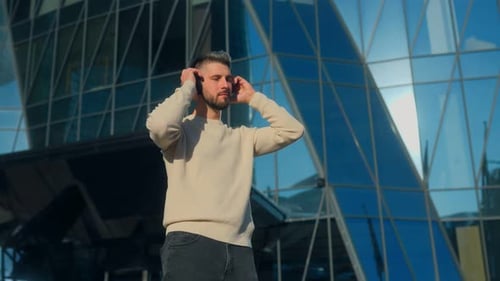 Young Bearded Man Listening to Music with Headphones in City