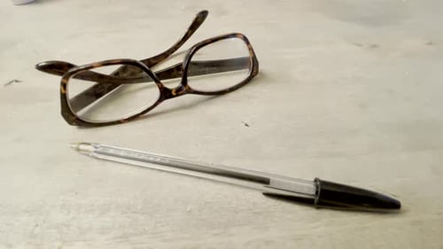 Reading glasses and a black ball point pen sitting on a table top.