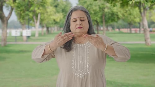 Relaxed Indian old woman doing breathe in breathe out exercise in park