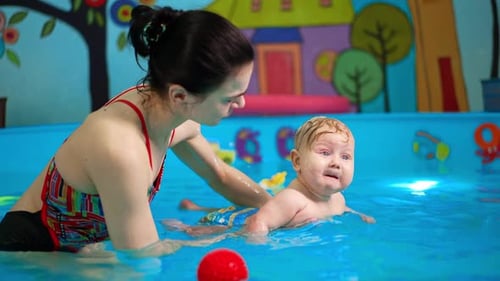 Caucasian brunette woman is holding a baby in the swimming pool.