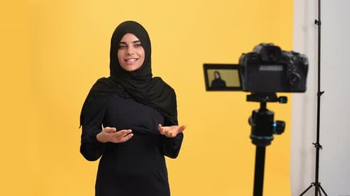 Smiling Muslim Woman in Black Hijab Talking Shooting Video Use Camera Posing Isolated Orange Studio