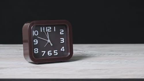 El reloj puntero sobre mesa de madera y fondo negro muestra la hora