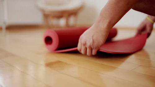 Male Hands Unfolding Red Yoga Mat on Wooden Floor
