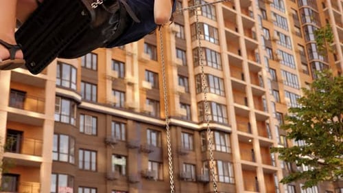 A Girl Rides on a Swing in the Courtyard of a Multistorey Residential Building