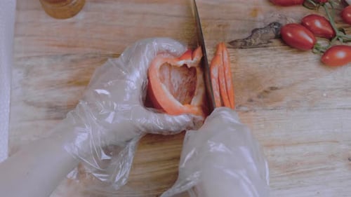 Front View of the Young Chef Cut Thin Slices of a Piece of Red Pepper with a Knife on the Cutting