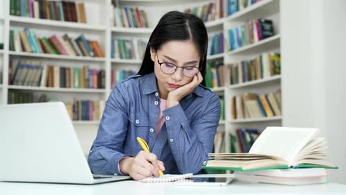 Busy asian female student tired of doing homework sitting at university library. Exhausted girl
