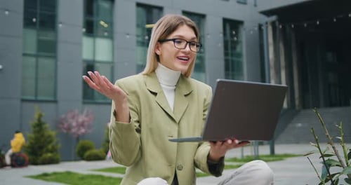 Woman in glasses having conference call on laptop with sitting on street near business centre