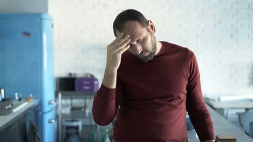 Man Suffering Headache in Kitchen Rubbing Temples
